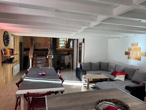 A cozy living room with a dining area, wooden walls, a fireplace, and a sofa.