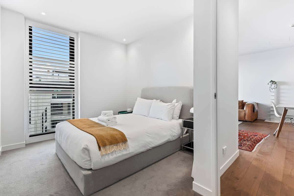 A modern bedroom with a large bed, a nightstand, and a window with blinds.