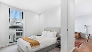 Een moderne slaapkamer met een groot bed, een nachtkastje en een raam met jaloezieën.