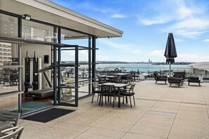 A rooftop terrace with exercise equipment, outdoor seating, and a view of the water. - Sleeps 4! + Parking, Pool and Gym by Zodiak Stays (Central Auckland)