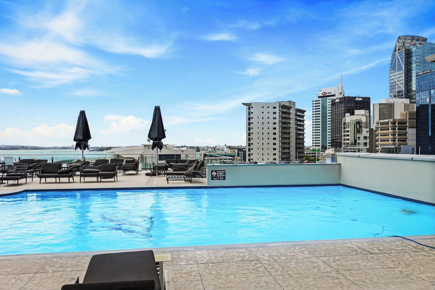 A rooftop pool with lounge chairs and umbrellas, surrounded by high-rise buildings.