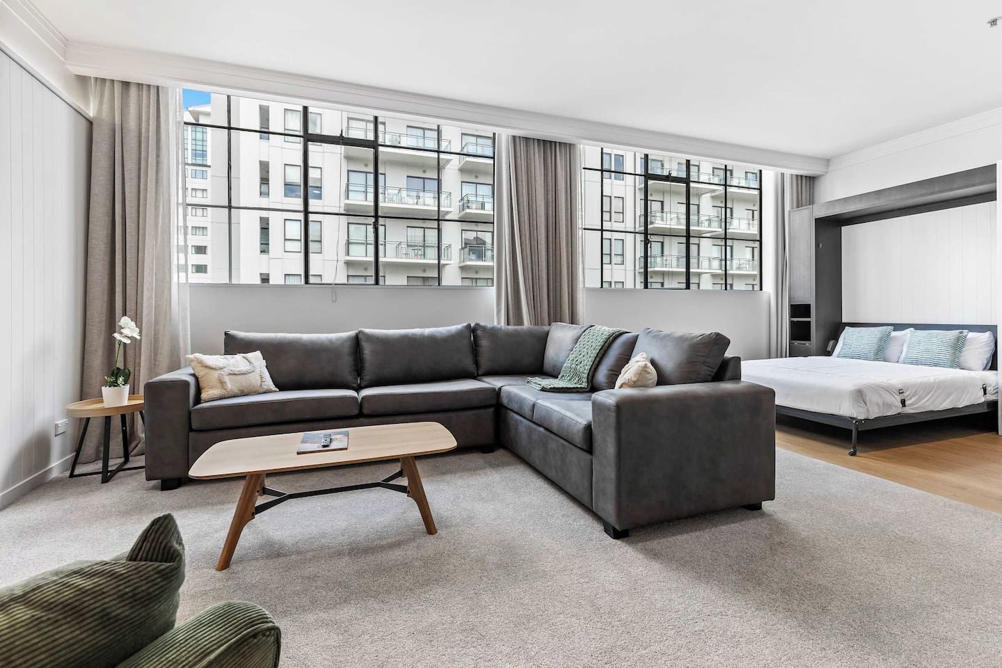 A modern living room with a sectional sofa, a small coffee table, and a bed with a headboard.