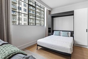 A modern bedroom with a bed, a wardrobe, and a view of a high-rise building. - Sleeps 4! + Parking, Pool and Gym by Zodiak Stays (Central Auckland)