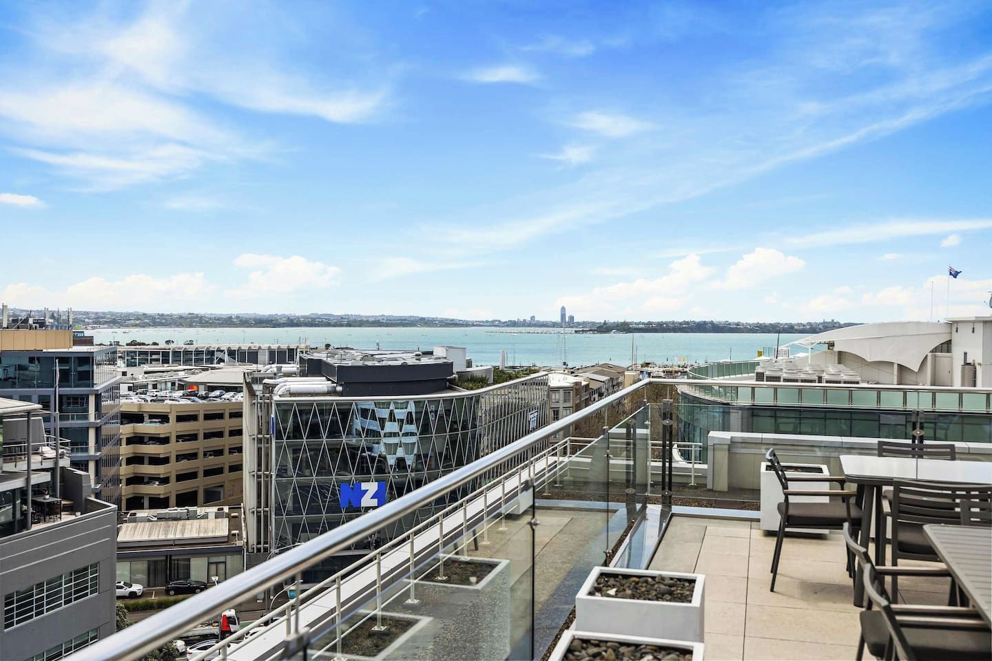 Une terrasse sur le toit offrant une vue sur la mer, des bâtiments modernes et un ciel dégagé.
