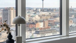 Ein Zimmer mit großem Fenster und Blick auf die Stadt, einem weißen Nachttisch und einer Lampe.