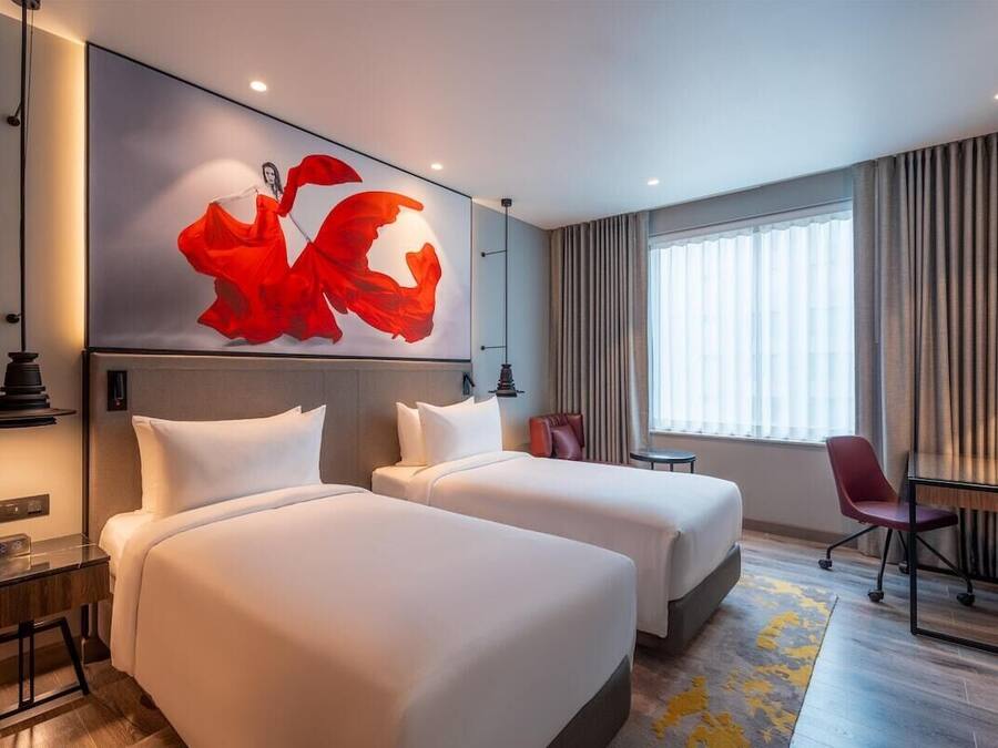 Habitación de hotel con dos camas, un escritorio, una silla y un cuadro abstracto grande en la pared.