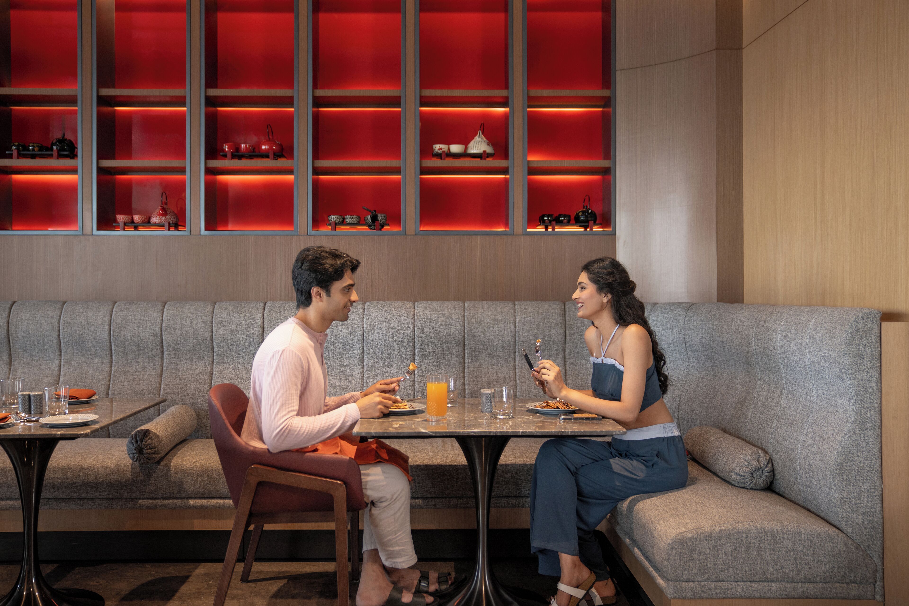 A modern dining area with a sofa and a table, a red-lit display case, and a neutral-toned wall.