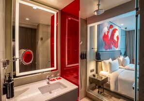 A modern hotel bathroom with a large mirror, a white sink, and a shower area.