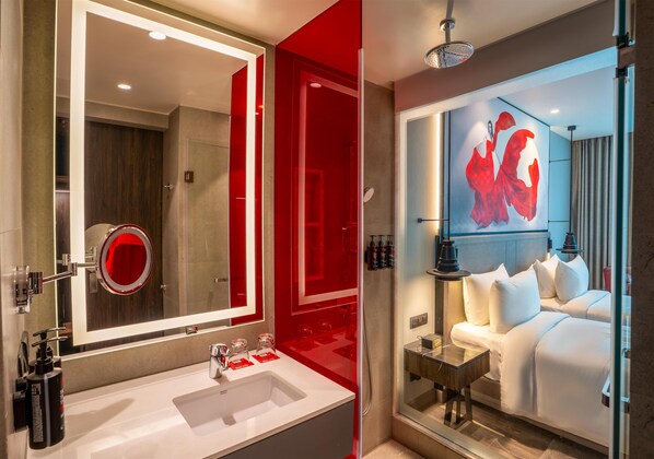 Un baño de hotel moderno con un espejo grande, un lavabo blanco y una zona de ducha.