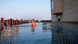 A swimming pool with a person in the water, a building with large windows, and a clear sky. - Radisson RED Indore (Indore)