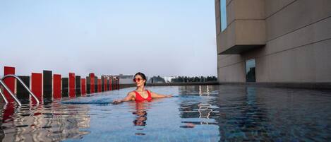 A swimming pool with a person in the water, a building with large windows, and a clear sky.
