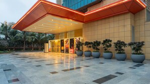 A modern hotel entrance with a geometric glass facade, large potted plants, and a tiled plaza. - Radisson RED Indore (Indore)