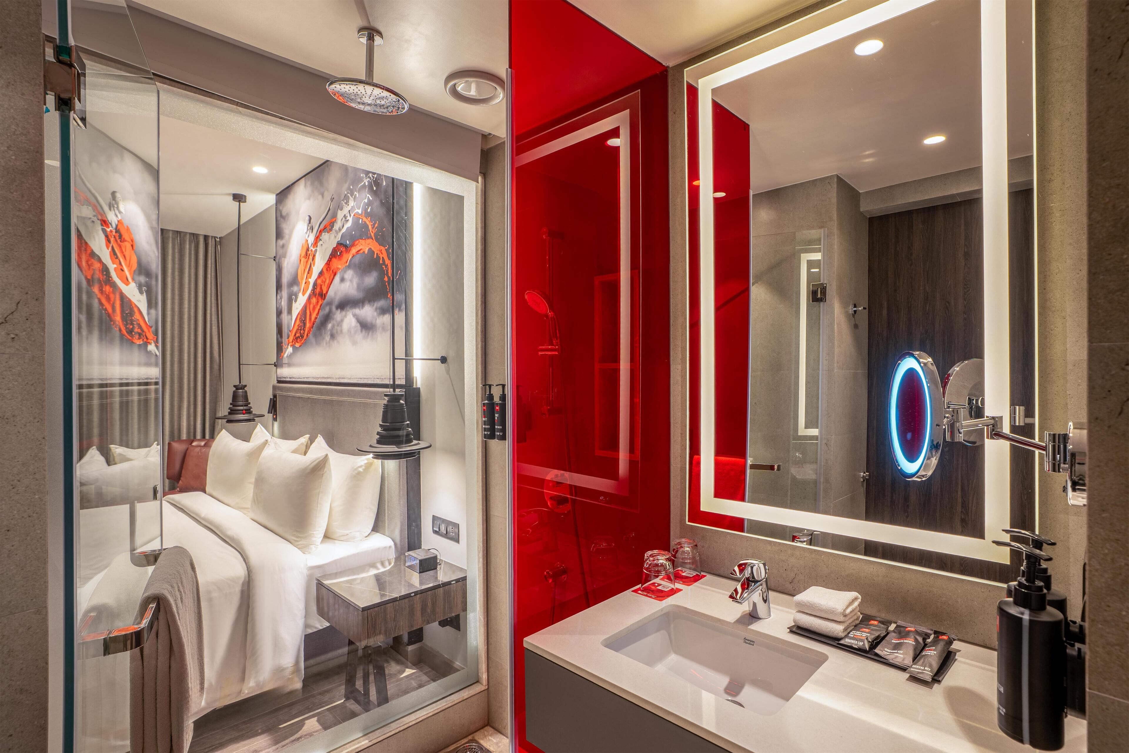 A modern hotel bathroom with a large mirror, a white sink, and a glass-enclosed shower area.