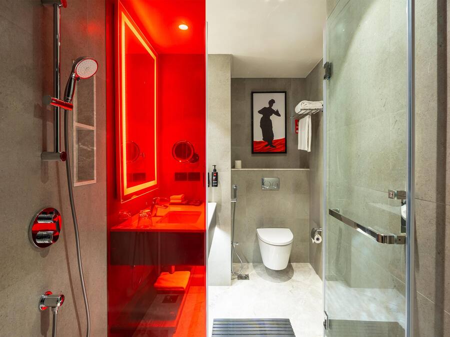 Un baño moderno con cabina de ducha de vidrio, un inodoro blanco y una zona de tocador iluminada con luz roja.