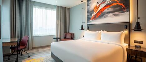A hotel room with a large bed, a desk, a chair, and a painting on the wall.