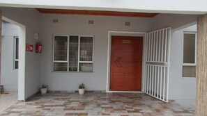 A building entrance with a red door, a window, and a fire exit sign. - Lilly Petals Guest House (Maun)
