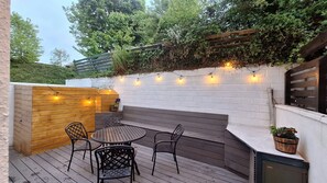An outdoor patio with a wooden table and chairs, a white brick wall, and string lights. - Greenway Getaway. Lovely central 3-bedroom townhome in peaceful Westport (Westport)