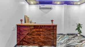 A reception area with a wooden desk, a ceiling fan, an air conditioning unit, and a potted plant. - Hotel Awadh Pearl (Lucknow)