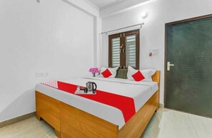 A neatly made bed with a red and white bedspread, a wooden headboard, and a small table with a kettle and a vase of flowers. - Hotel Awadh Pearl (Lucknow)