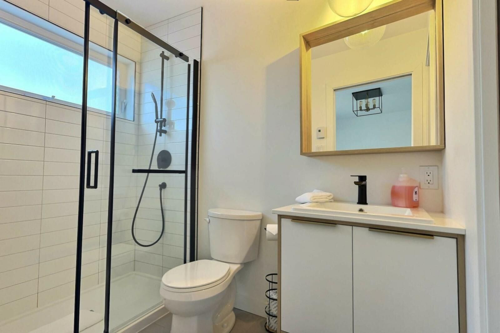 Un baño moderno con ducha envuelta en vidrio, inodoro blanco y tocador con espejo.