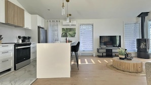 Una cocina moderna con una isla central, un área de comedor con televisión y una zona de estar acogedora con chimenea.