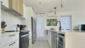 Una cocina moderna con una isla central, electrodomésticos de acero inoxidable y vistas al exterior a través de un ventanal.