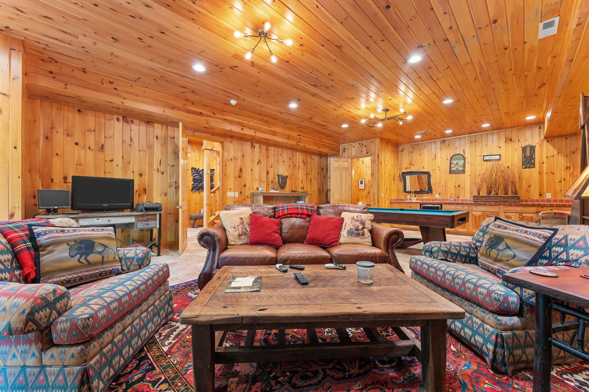 A cozy wooden interior with a pool table, leather sofas, and a television.
