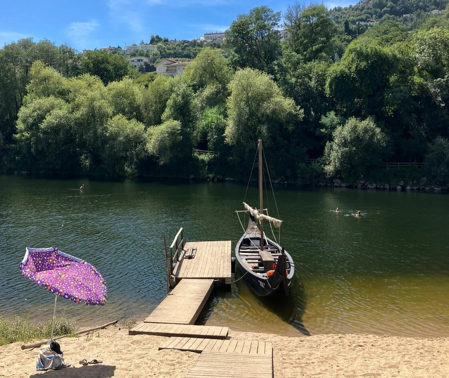 Un muelle de madera se extiende sobre un río tranquilo, rodeado de densa vegetación y un cielo despejado.