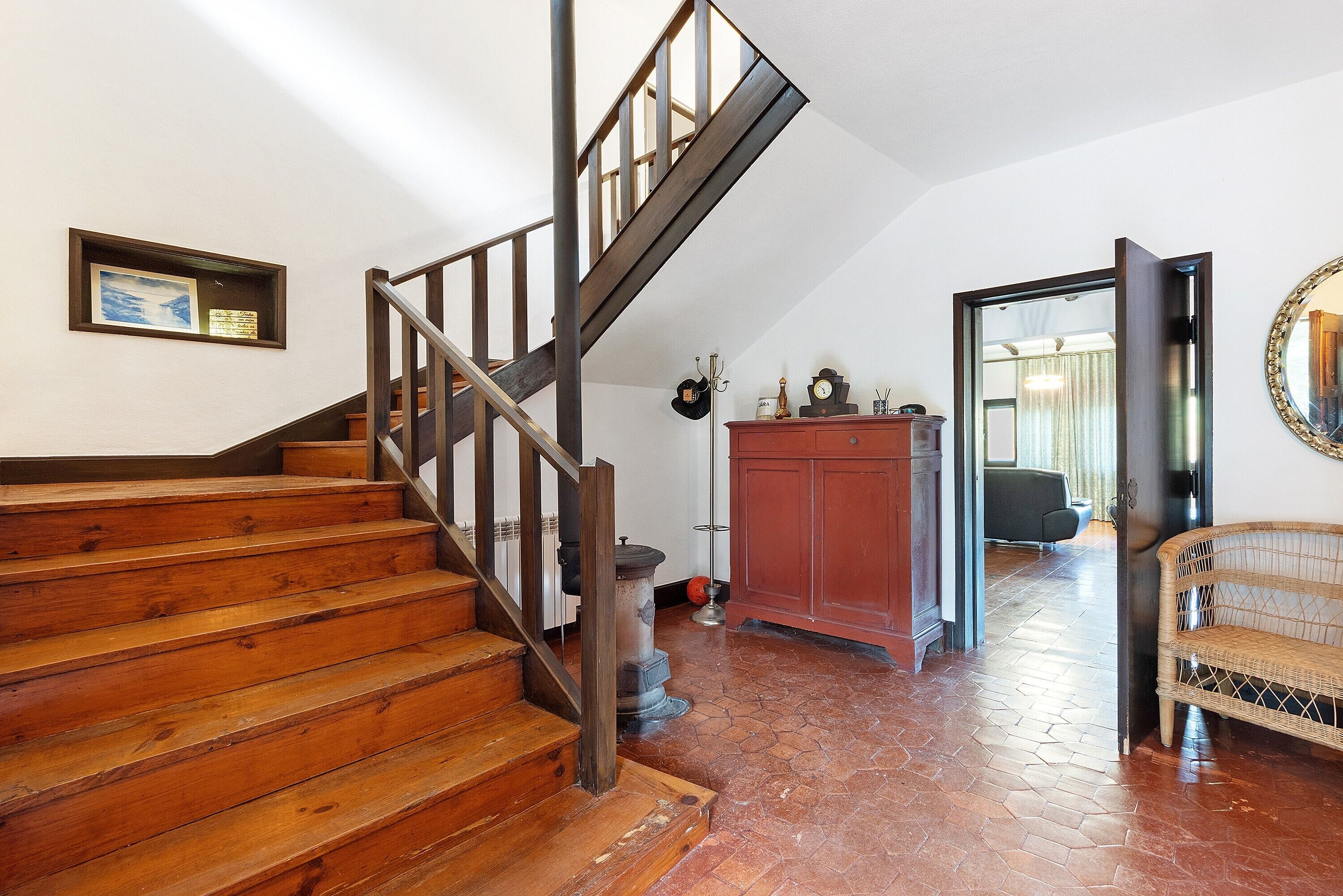 A staircase with wooden steps and a metal railing, leading to a room with a red cabinet and a wicker sofa.