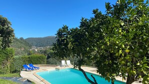 Une piscine à l’eau d’un bleu limpide, entourée de verdure et avec des collines en arri ère-plan.