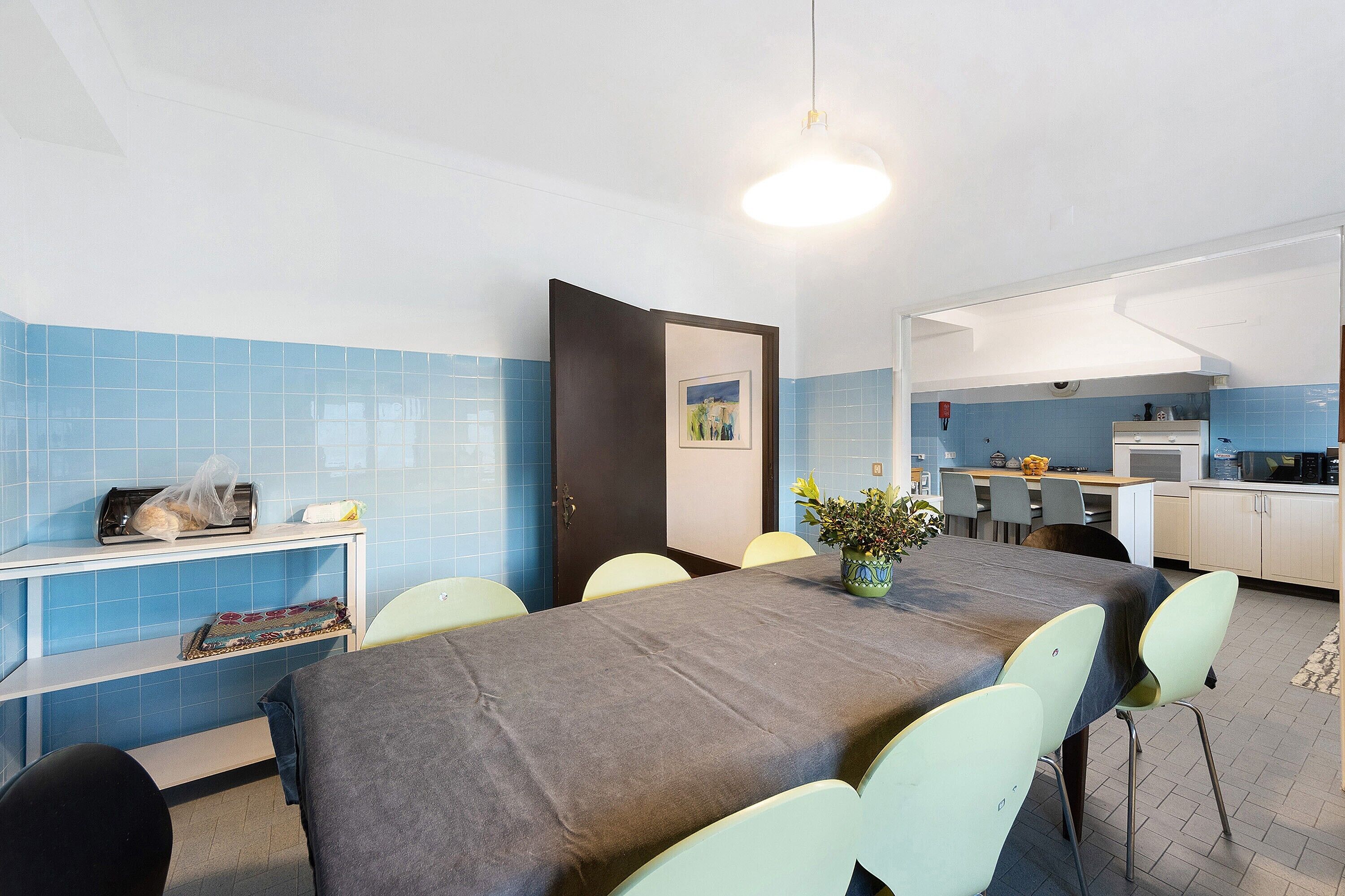 A modern kitchen with blue tiles, a dining table with chairs, and a small seating area with a bench.