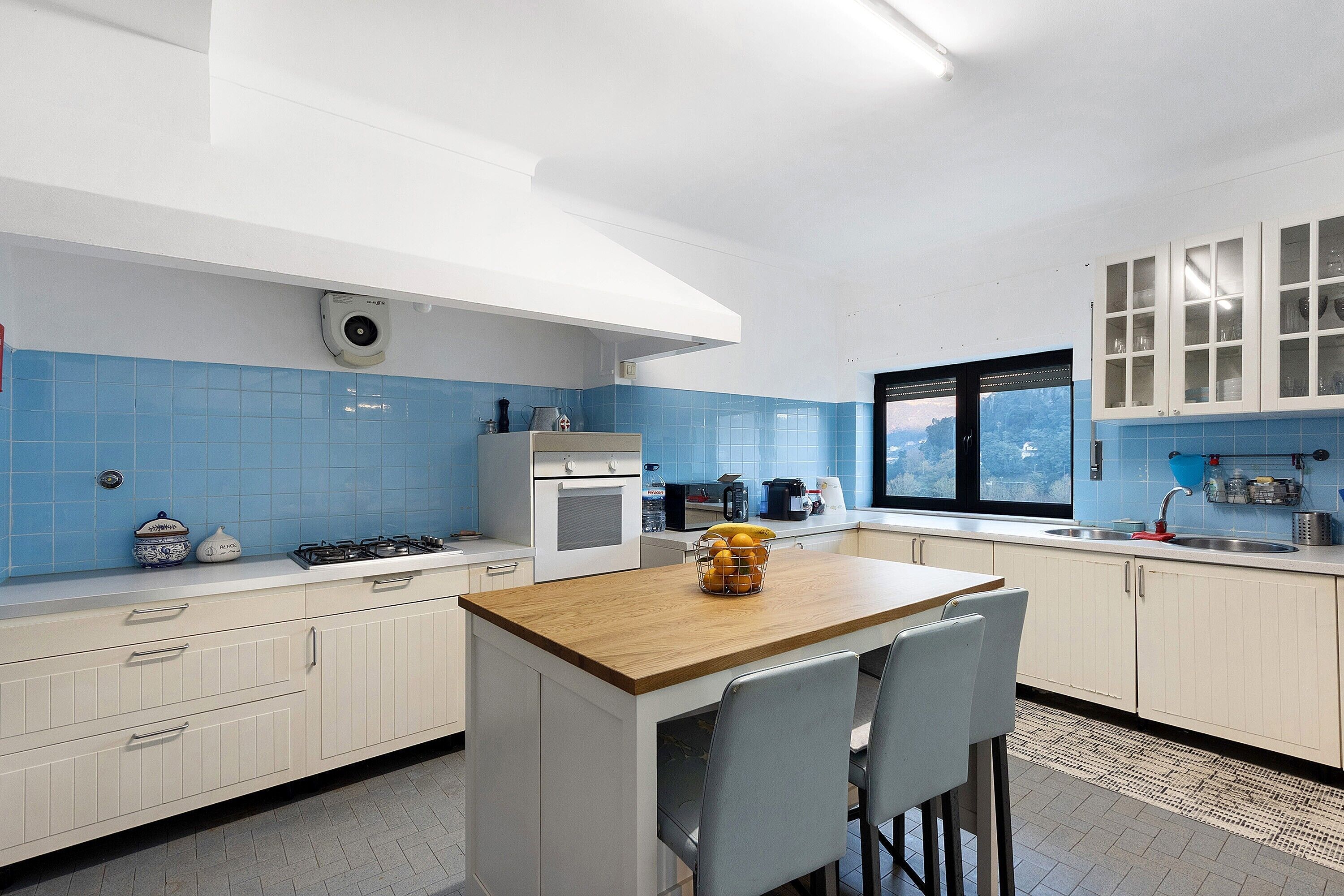 Et moderne køkken med en central ø, hvide skabe, blå fliser og et vindue med udsigt.