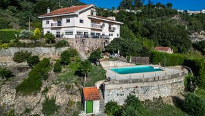 Une grande maison à plusieurs étages, dotée d’une piscine, entourée de verdure et de collines.