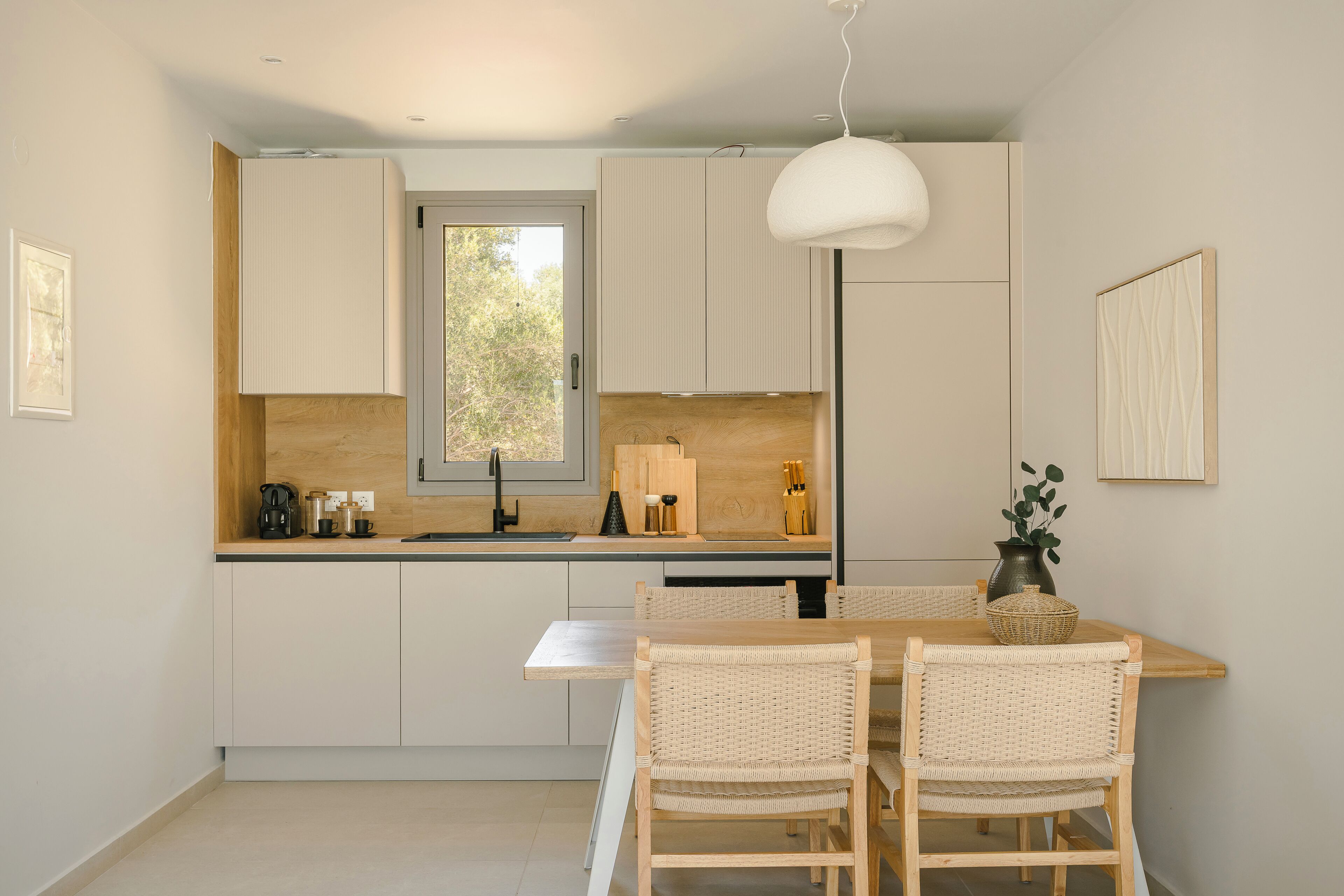 Eine moderne Küche mit weißen Schränken, einer Holz Arbeitsplatte, einem Esstisch mit Korbstühlen und einer hängenden Pendelleuchte.