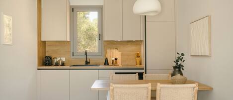 A modern kitchen with white cabinets, a wooden countertop, a dining table with wicker chairs, and a hanging pendant light.