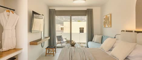 Ein modernes Hotelzimmer mit einem Bett, einer Sitzecke mit Tisch, einem ausgelegten Bademantel und Blick ins Freie.