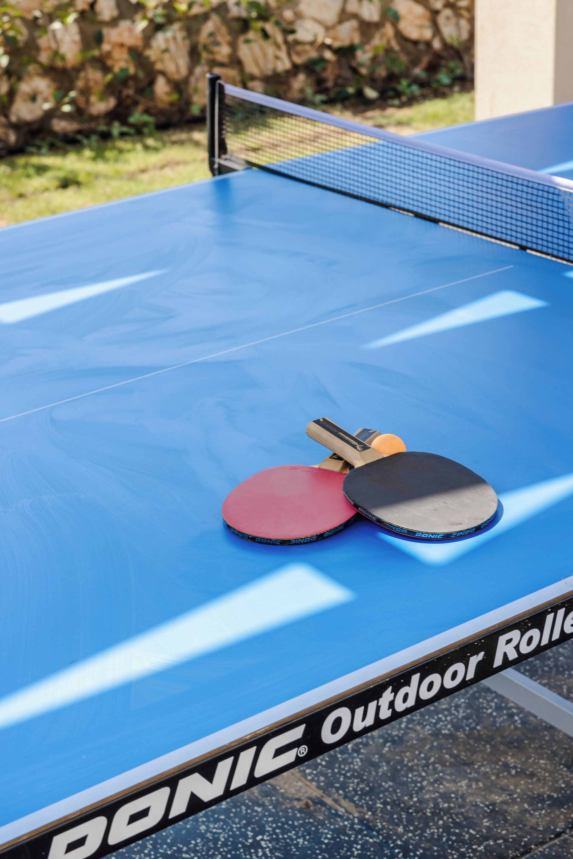 A blue table tennis table with two paddles and a net.