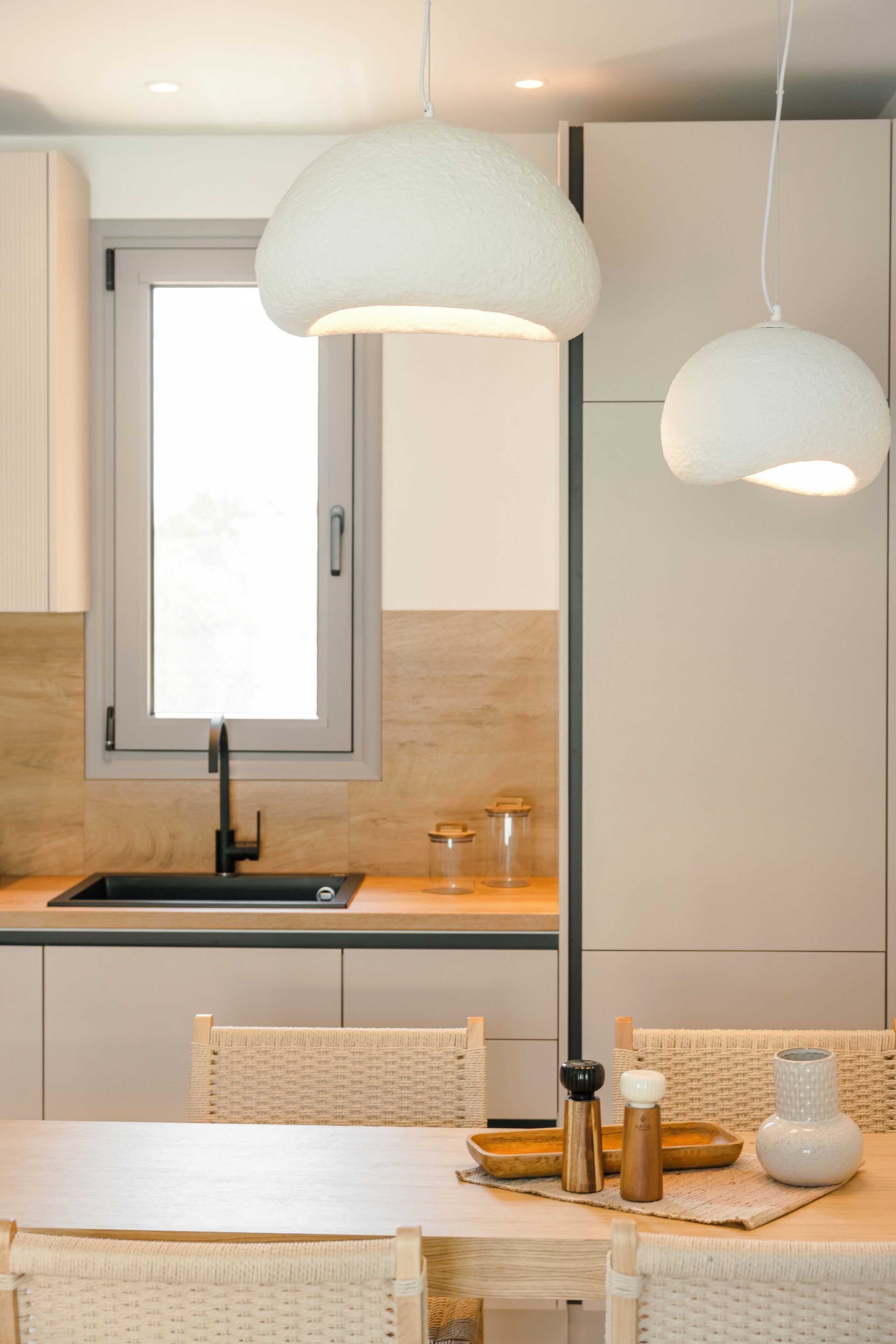 A modern kitchen with a window, white pendant lights, and a dining area with wicker furniture.