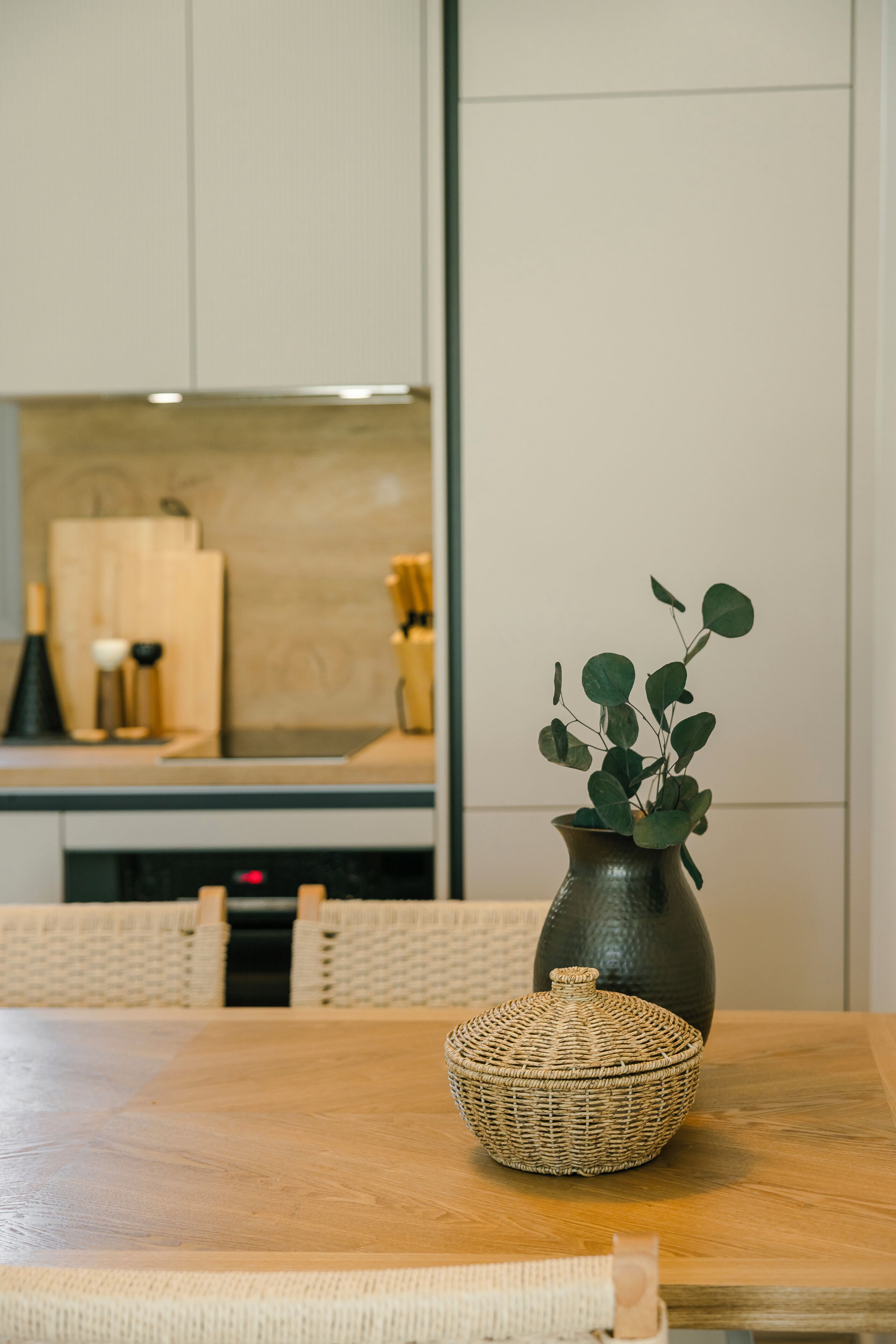 A dining table with a woven basket and a vase with green leaves.