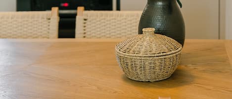 A dining table with a woven basket and a vase with green leaves.