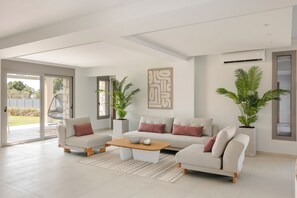 A spacious living room with a large sofa set, a coffee table, and two potted plants. - Ionian Treasure Suites (Kefalonia)