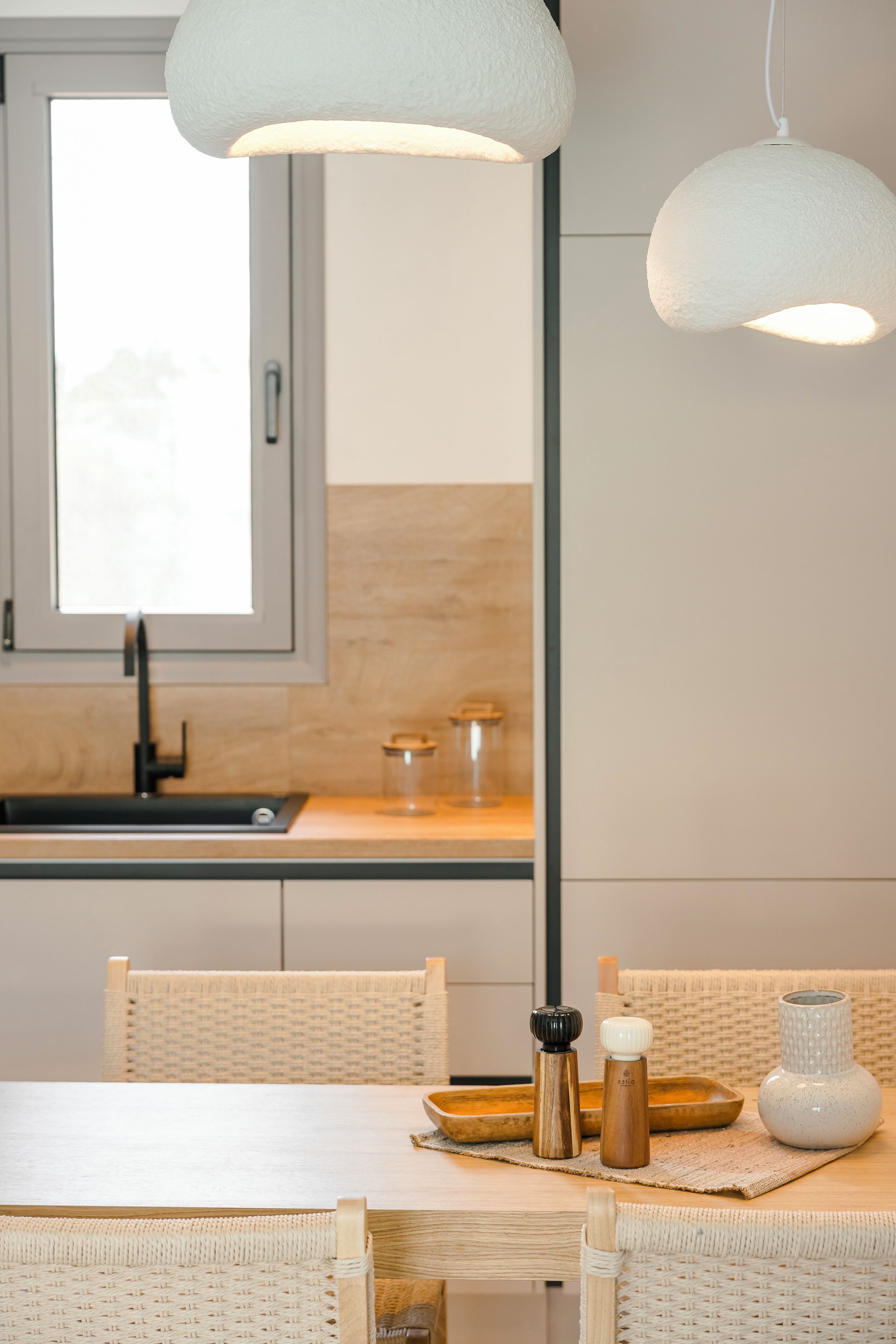 A modern kitchen with a window, a sink, and a dining area with wicker chairs and a table.