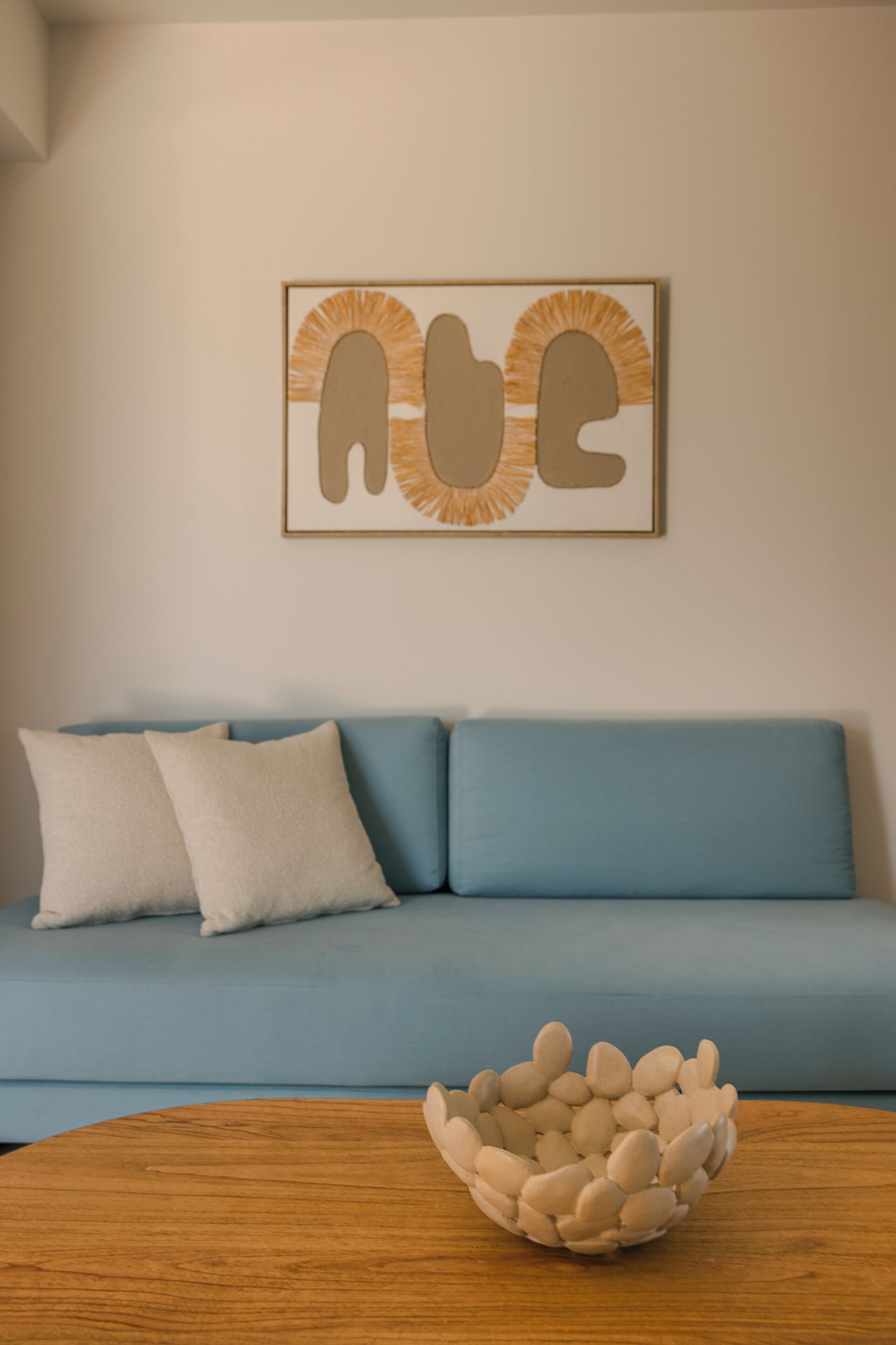 Una habitación con un sofá azul, dos almohadas blancas y una mesa de madera con un tazón blanco.