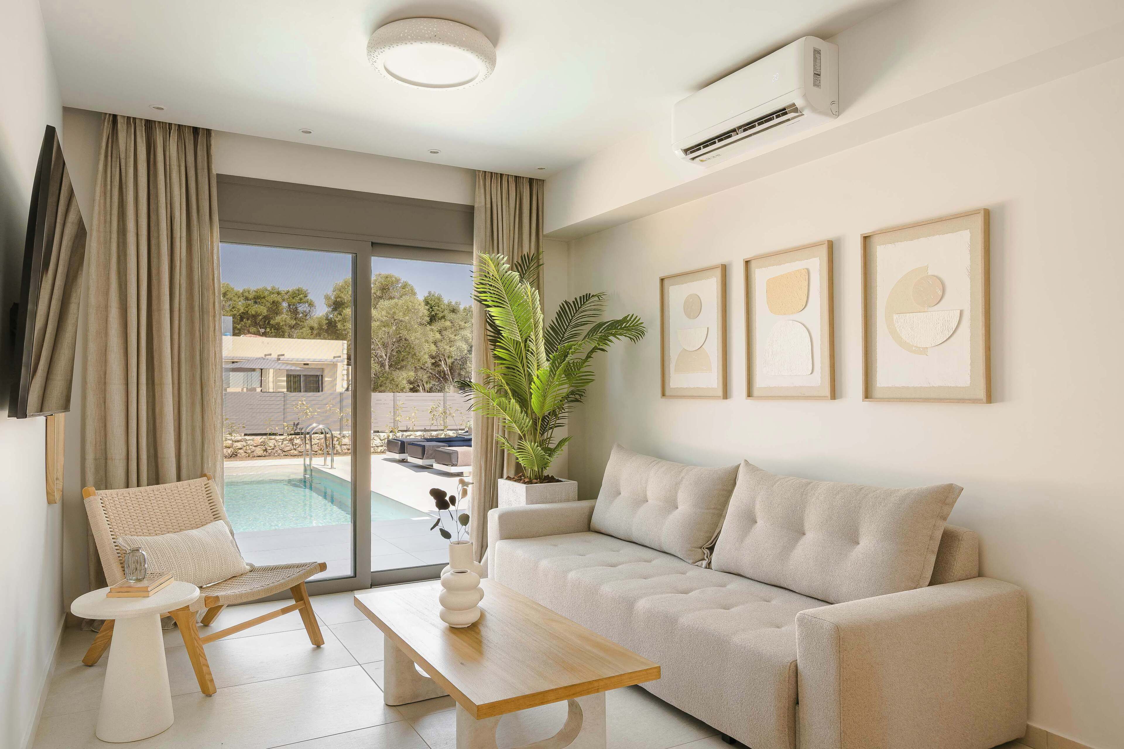 A modern living room with a sofa, a chair, a coffee table, and a large window with a view of a swimming pool and greenery.