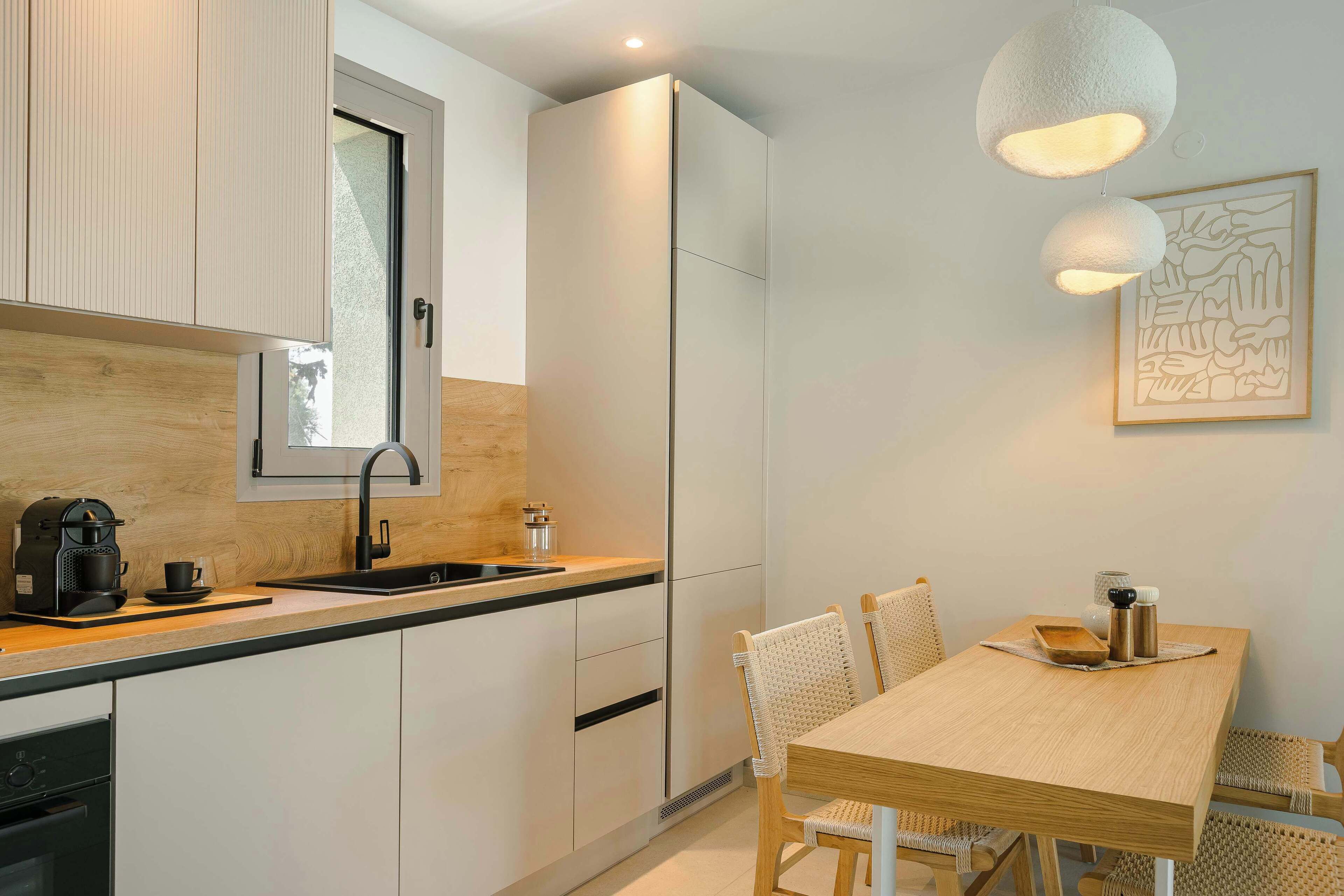 A modern kitchen with white cabinets, a wooden countertop, a sink, and a dining area with a wooden table and wicker chairs.