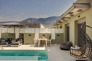 Zona junto a la piscina con sillas de descanso, una mesa y un sillón colgante.