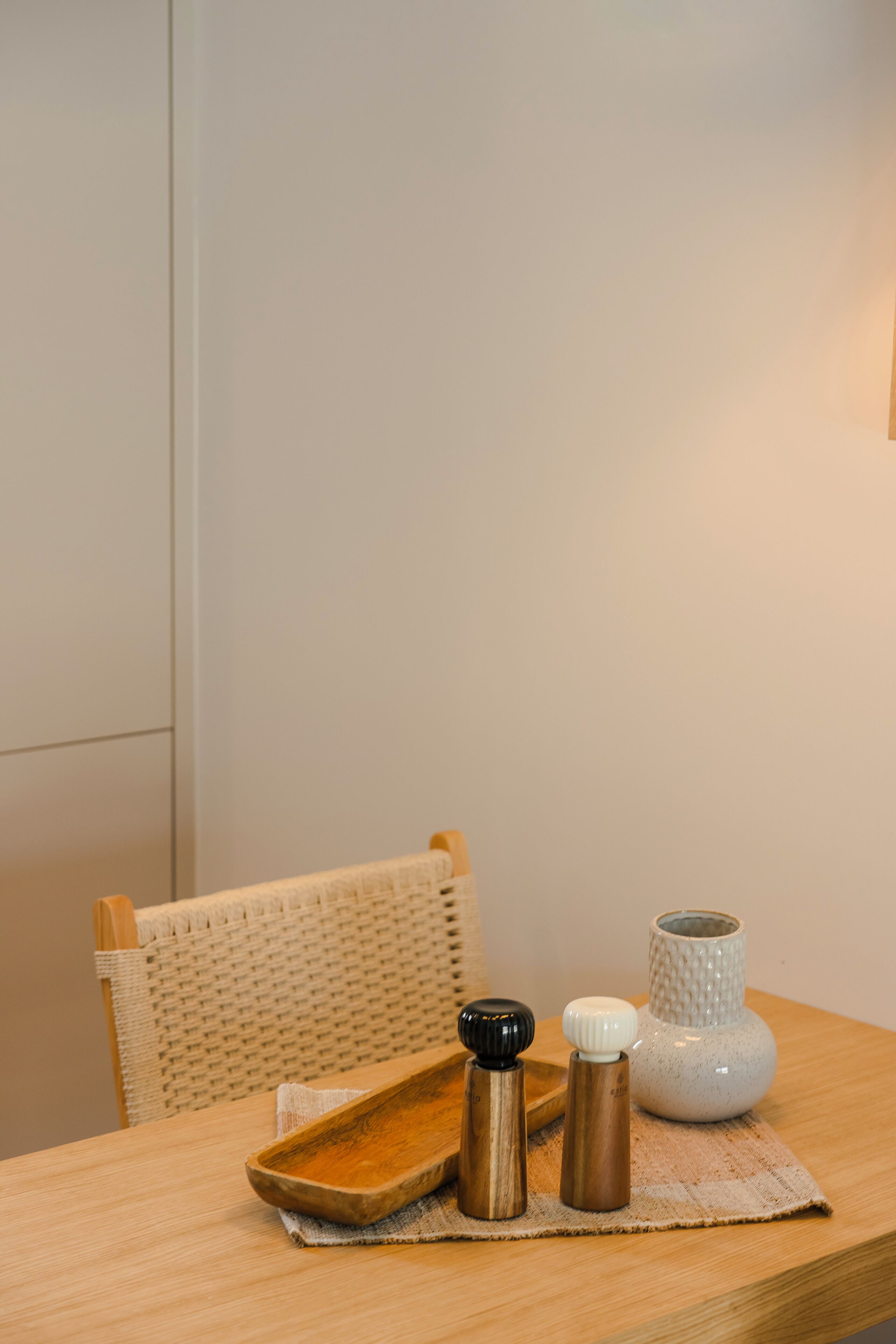 A wooden table with a woven chair, a tray, and two salt and pepper shakers.