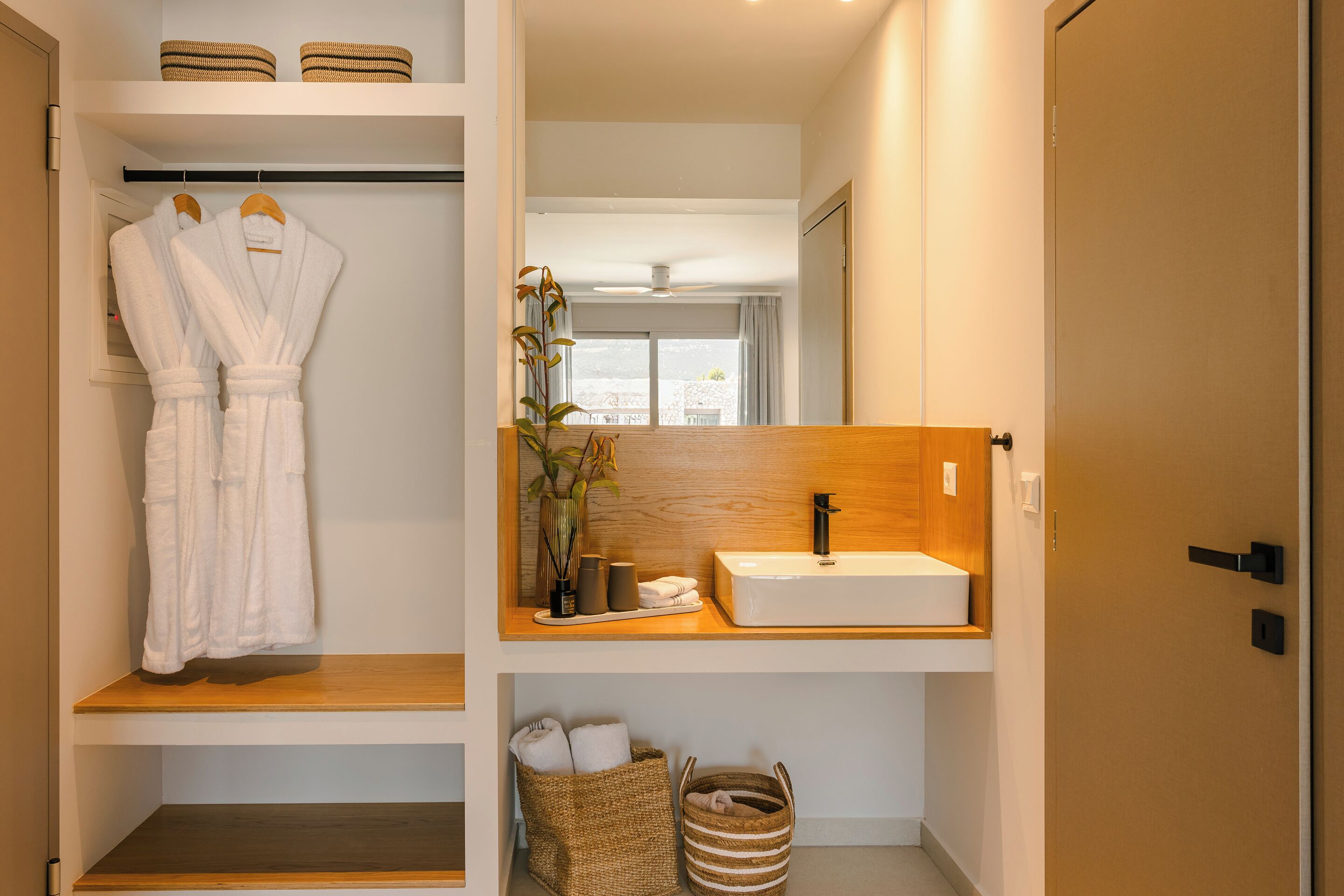 A bathroom with a wooden vanity, a white sink, and two white robes hanging on a rack.