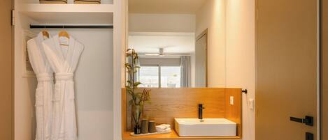 A bathroom with a wooden vanity, a white sink, and two white robes hanging on a rack.