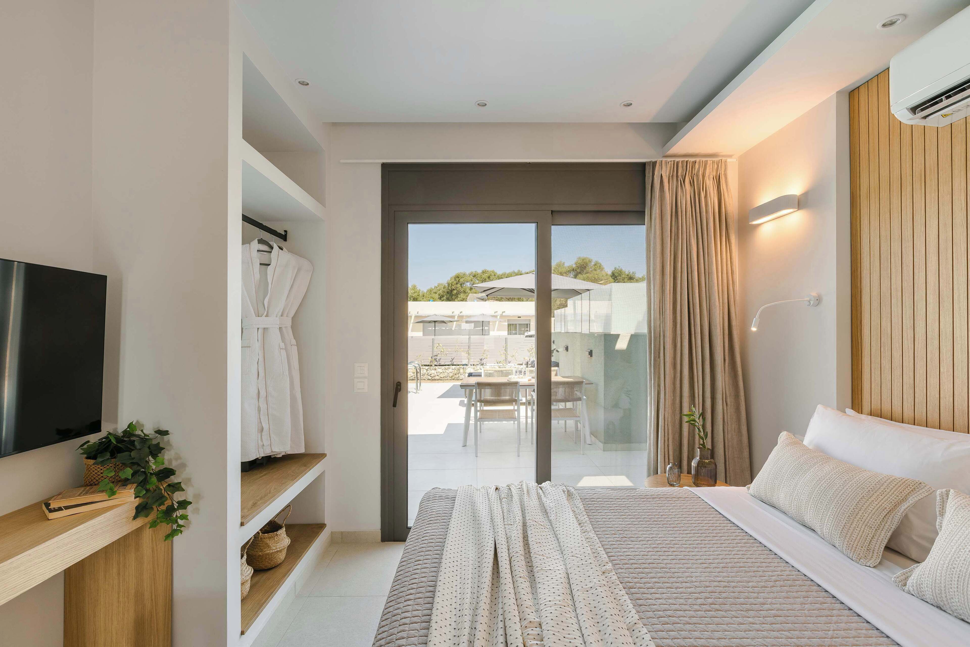 Een moderne slaapkamer met een groot bed, een televisie, een kledingkast en een schuifdeur naar een balkon.